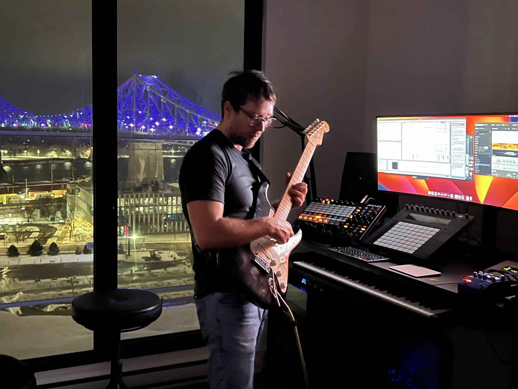 Vincent Cantin Bellemare à la guitare dans son studio, le pont Jacques-Cartier illuminé derrière
